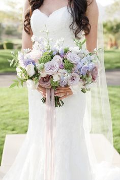 a woman in a wedding dress holding a bridal bouquet with purple and white flowers