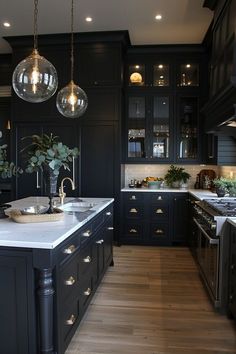 a large kitchen with black cabinets and marble counter tops, two pendant lights hanging from the ceiling