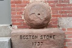 a brick wall with the name boston stone on it and a large rock in front of it