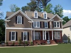 a two story house with black shutters and white trim on the windows, along with green grass