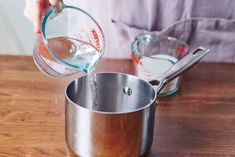 a person pouring water into a pot on top of a wooden table next to measuring cups