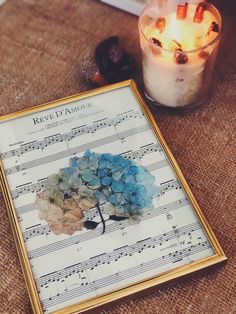 a lit candle sitting on top of a table next to sheet music and a flower arrangement