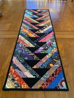 a long table runner made out of quilts on top of a wooden floor with chairs in the background