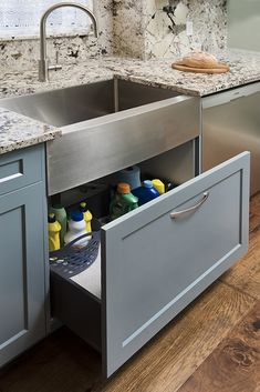 the kitchen sink is open and has cleaning products in its storage drawer under the faucet