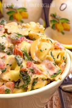 a pasta dish with ham and spinach in a white bowl on a wooden table