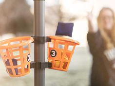 a woman standing next to a pole with two baskets hanging from it's sides