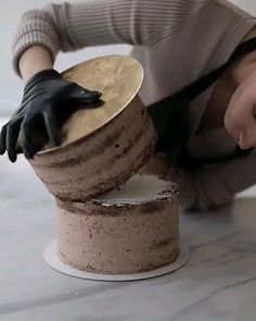 a woman bending over to place a chocolate cake on top of a round cake plate