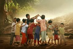 a group of children standing next to each other in front of a tree and dirt field