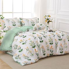 a white bed with yellow flowers and green leaves on the comforter is in front of a window