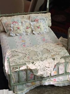 an old fashioned doll bed with white lace and flowers on it's coverlet