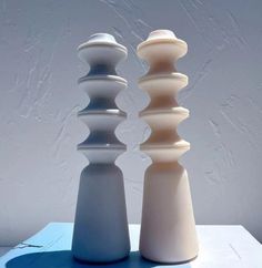 three white and gray vases sitting on top of a blue table next to each other