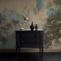 a black dresser with two vases on it and a gold lamp next to it