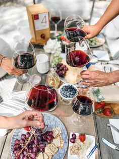 several people are toasting wine glasses at a table with grapes and crackers on it