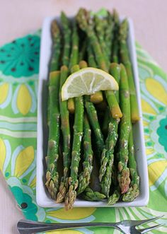 asparagus with lemon wedges in a white dish on a green and yellow tablecloth