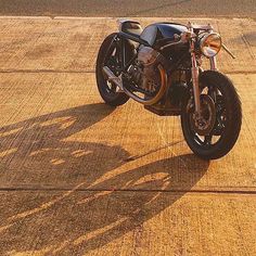 the motorcycle is parked on the side of the road with its shadow in the pavement