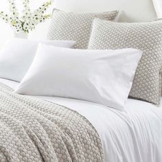 a bed with white sheets and pillows on top of it next to a vase filled with blue flowers