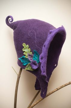 a close up of a purple hat on top of a branch with leaves and flowers