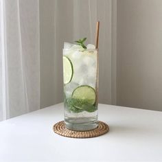 a tall glass filled with ice and cucumber on top of a white table