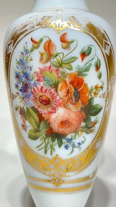 a white vase with flowers painted on the side and gold trimming around the edges