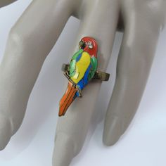 You'll get Lucky in more ways than one when this ring flies in for it's not only the break but the brand! For your Parrot pleasure we offer this rascally ring, made of bronzed metal with hand applied enamels in red, green, yellow, orange and blue with a sparkling clear rhinestone gleaming from the Bird's eye. The Parrot is elongated (which is so slenderizing for the fingers) and measures 1 3/8 inches long, 3/8 inch wide and is a size 6.75. It is in good vintage condition and marked Lucky Brand o Get Lucky, Tropical Bird, Christmas Bird, Chunky Bracelets, Bird Earrings, Bird Brooch, Bird Jewelry, Bird Lover, Tropical Birds