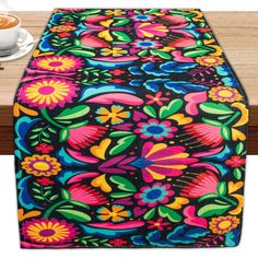 a colorful table runner on top of a wooden table next to a cup of coffee