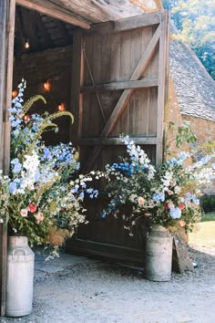 two buckets filled with flowers sitting in front of a barn