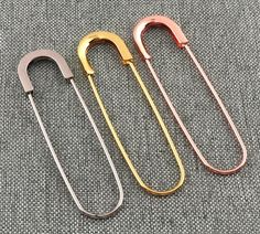 three different colored metal hair pins on a gray surface, one is gold and the other is silver