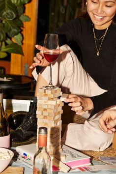 a woman holding a wine glass next to a tower of blocks