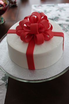 a white cake with a red bow on top sitting on a glass platter next to a table