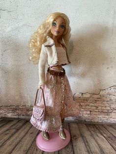 a barbie doll is standing on a pink base holding a purse and wearing a dress