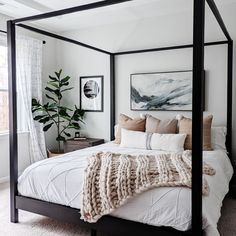 a bedroom with a four poster bed, white walls and carpeted flooring that has a painting on the wall