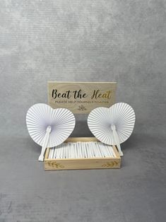 two white paper fans sitting on top of a wooden box next to a sign that says beat the heat