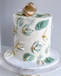 a wedding cake decorated with gold and green leaves on a white tableclothed stand