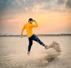 a man in yellow shirt kicking up sand on beach