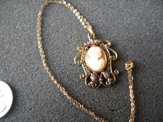 "This is listing is for a vintage cameo on a 16 inch chain. I bought this from an estate sale, I know no history. The cameo setting and chain are both marked \"120D12K\", as best as I can detect. The chain is marked on the clasp. The cameo background is thin, as detected when held up to a light. It has lovely features. There is corsage or floral detail on one shoulder. The setting is quite lovely with scroll and leaf design. Nice detail Please view pictures for more details. This item will be wr Vintage Cameo, Vintage Americana, Cameo Necklace, View Pictures, Grab Bags, Leaf Design, Pearl Beads, Estate Sale, Vintage Gold