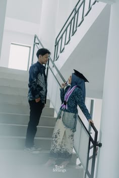 a man and woman standing on the stairs in front of a stair case while looking at each other