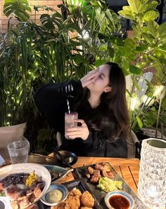 a woman sitting at a table with food and drinks in front of her, looking up into the air