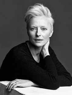 a black and white photo of a woman with her hand on her chin looking at the camera