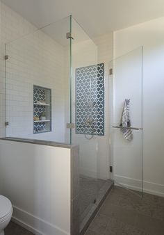 a bathroom with a glass shower door, toilet and tiled walls in the back ground