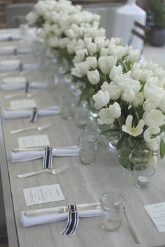 a long table with white flowers and silverware on it, along with place cards