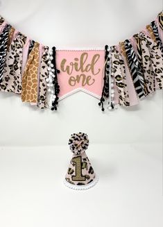 a birthday banner that says wild one on it with a giraffe print and pom poms