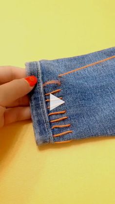 a woman's hand holding onto a pair of blue jeans with orange stitching