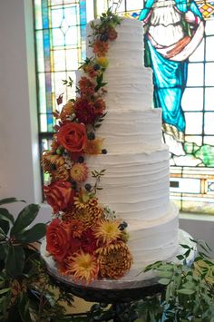 a white wedding cake with flowers on top and stained glass window in the back ground