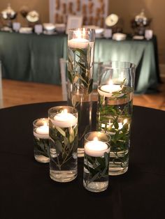 candles are placed in glass vases with greenery