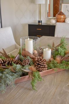 a wooden tray filled with pine cones, candles and greenery on top of a table