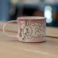 a pink coffee cup sitting on top of a wooden table