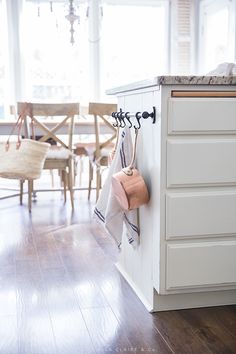 a kitchen with white cabinets and wooden floors, hanging towels on hooks from the wall