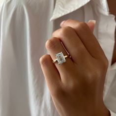 a woman's hand with a diamond ring on her left hand, wearing a white shirt