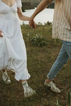 a man and woman holding hands walking in the grass