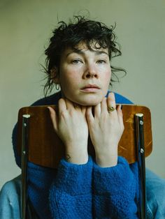 a woman sitting in a chair with her hands on the back of her head and looking at the camera